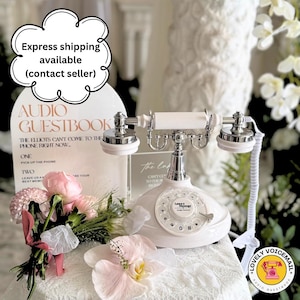 Pu&ograve; includere: Un telefono bianco in stile vintage con quadrante rotante e dettagli argentati. Il telefono fa parte di un'impostazione di libro degli ospiti audio, con un cartello che recita "Audio Guestbook". Sono visibili anche un bouquet di fiori rosa e un adesivo "Lovely Voicemail".