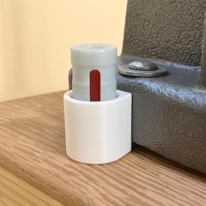 May include: A white, cylindrical object with a red stripe is held in a white holder. The holder is next to a gray metal object. The items are on a wooden surface.