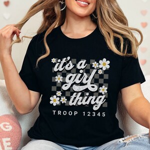 May include: Black t-shirt with a white graphic that says "it's a girl thing" with a checkered background and daisies. The text "TROOP 12345" is below the graphic.