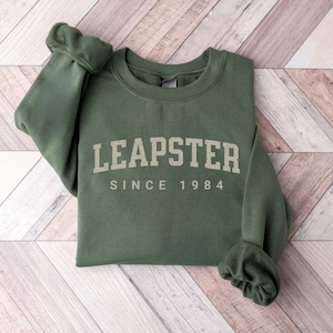May include: A green sweatshirt with the text "LEAPSTER SINCE 1984" in gold lettering.