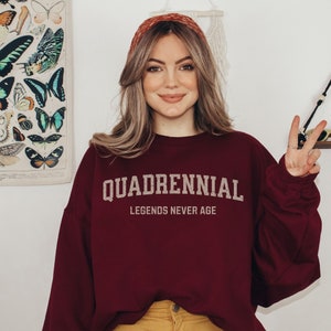 May include: A maroon sweatshirt with the text "Quadrennial Legends Never Age" in white lettering.