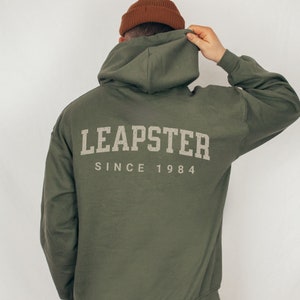 May include: A green hooded sweatshirt with the text "LEAPSTER SINCE 1984" printed on the back.