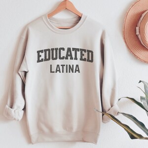 May include: A beige sweatshirt with the text "EDUCATED LATINA" printed in black.