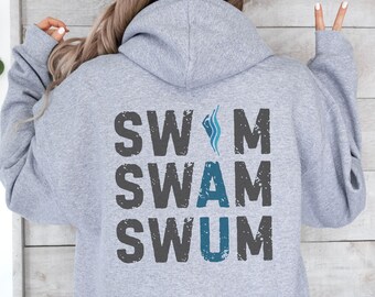 Op de afbeelding: Grijs hooded sweatshirt met de woorden "SWIM SWAM SWUM" gedrukt op de rug in zwart met een distressed look. De woorden zijn verticaal gestapeld met een blauwe golfgrafiek tussen de eerste twee woorden.