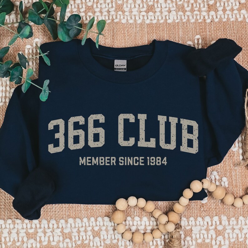 Op de afbeelding: Donkerblauwe sweatshirt met de tekst "366 CLUB MEMBER SINCE 1984" in wit.