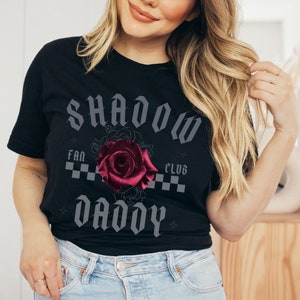 May include: Black t-shirt with a graphic design featuring a red rose and the text "Shadow Fan Club Daddy" in a gothic font.