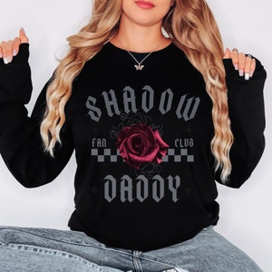May include: Black sweatshirt with a graphic print of a red rose and the text "Shadow Fan Club Daddy" in a gothic font.