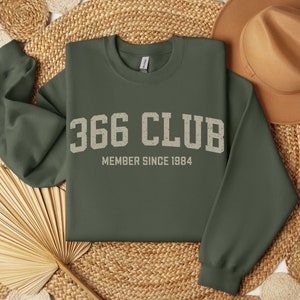 Op de afbeelding: Een groen sweatshirt met de tekst "366 CLUB MEMBER SINCE 1984" in wit.