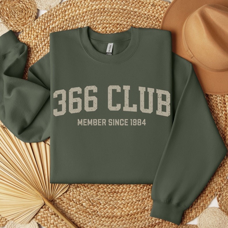 Op de afbeelding: Een groen sweatshirt met de tekst "366 CLUB MEMBER SINCE 1984" in wit.
