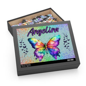 May include: A 120 piece 8x10 inch jigsaw puzzle featuring a colorful butterfly with a rainbow pattern on a blue background with glitter. The puzzle box has the name "Angelina" printed on it.