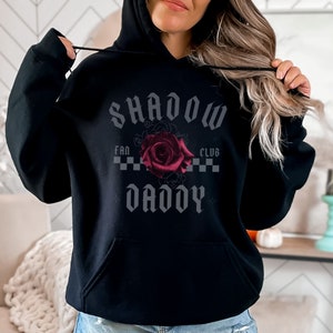 May include: Black hooded sweatshirt with the text "SHADOW DADDY" in a gothic font, a red rose, and the words "FAN CLUB" above the rose.