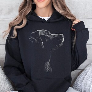 May include: A black hooded sweatshirt featuring a white line-art graphic of a dog in profile on the chest. The hoodie includes a front kangaroo pocket, long sleeves with ribbed cuffs, and a drawstring hood, providing a casual and functional garment.