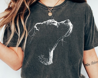 May include: A charcoal gray short-sleeve t-shirt featuring a white line-art graphic of a dog's head in profile looking upward. The shirt has a faded, vintage-style wash and the word PEPPER is printed in black in the upper right corner.