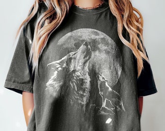 Könnte beinhalten: Ein anthrazitfarbenes Kurzarm-T-Shirt mit einem großen weißen Grafikdruck eines Wolfes, der den Vollmond anheult, sowie einem kleineren Wolf daneben. Das T-Shirt hat einen Rundhalsausschnitt und eine lockere, übergroße Passform.