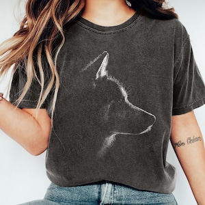 May include: A charcoal grey short-sleeve t-shirt featuring a white line-art graphic of a dog's profile on the chest. The shirt has a crew neckline and a faded, vintage-style wash. The design depicts the head and ears of a canine in silhouette.