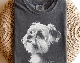 May include: A charcoal gray crew neck t-shirt featuring a detailed white line art illustration of a small, fluffy dog looking upward. The shirt has a visible brand label at the inner neckline and a classic short-sleeve design with a relaxed fit.