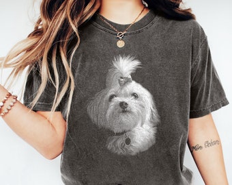 May include: A charcoal gray short-sleeve t-shirt featuring a white graphic illustration of a small, long-haired dog with a topknot bow. The shirt has a crew neckline and a vintage-style washed finish, paired with blue denim jeans and white sneakers.