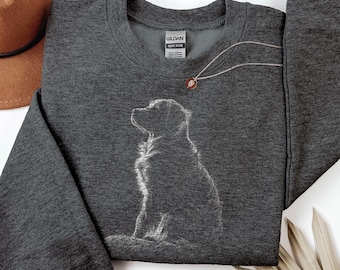 May include: A dark charcoal gray crewneck sweatshirt featuring a white line art illustration of a sitting dog on the front. The garment has long sleeves and a ribbed collar, with a Gildan brand label visible at the inner neckline of the shirt.