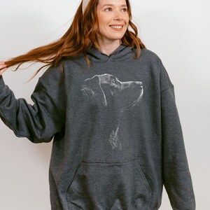 May include: A dark charcoal gray hooded sweatshirt featuring a white line art illustration of a dog's profile on the chest. The garment includes a front kangaroo pocket, long sleeves with ribbed cuffs, and a drawstring hood in a matching fabric.