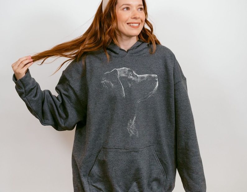 May include: A dark charcoal gray hooded sweatshirt featuring a white line art illustration of a dog's profile on the chest. The garment includes a front kangaroo pocket, long sleeves with ribbed cuffs, and a drawstring hood in a matching fabric.