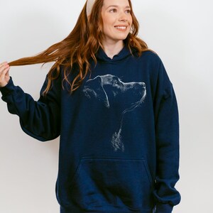 May include: A navy blue hooded sweatshirt featuring a white line art illustration of a dog's profile on the chest. The garment includes a front kangaroo pocket, long sleeves with ribbed cuffs, and a drawstring hood, providing a casual look.