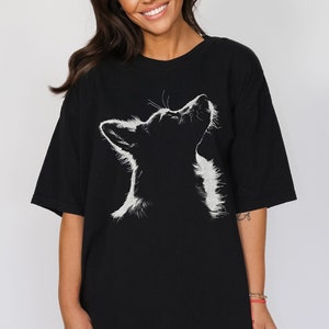 May include: A black short-sleeved t-shirt featuring a white graphic illustration of a dog looking upward. The design highlights the silhouette of the dog's head and neck with detailed white fur textures against the solid black fabric of the shirt.