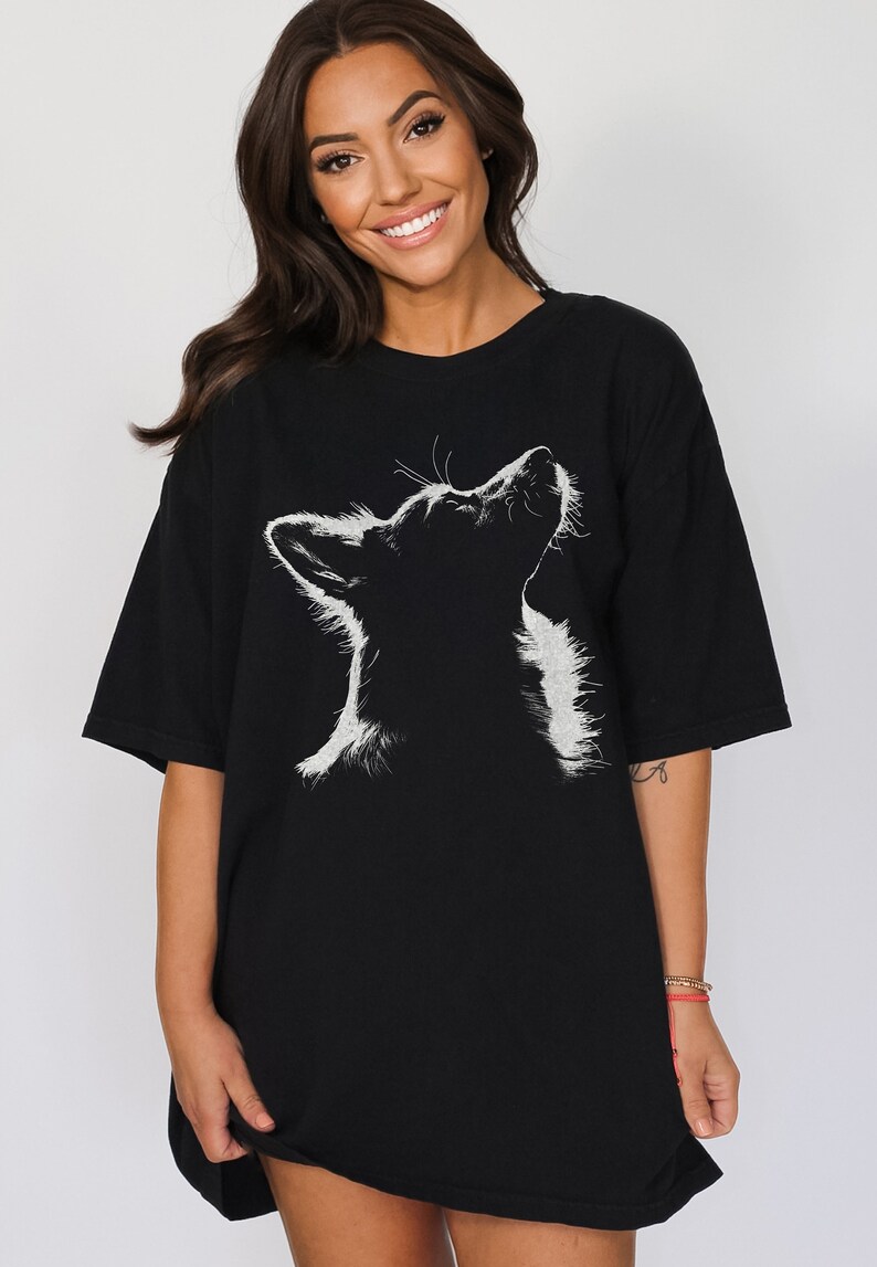 May include: A black short-sleeved t-shirt featuring a white graphic illustration of a dog looking upward. The design highlights the silhouette of the dog's head and neck with detailed white fur textures against the solid black fabric of the shirt.