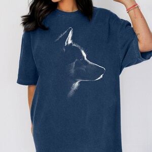 May include: A navy blue short-sleeved t-shirt featuring a white graphic print of a wolf head in profile. The design highlights the wolf's silhouette and facial features in a sketch-like style centered on the front of the garment.