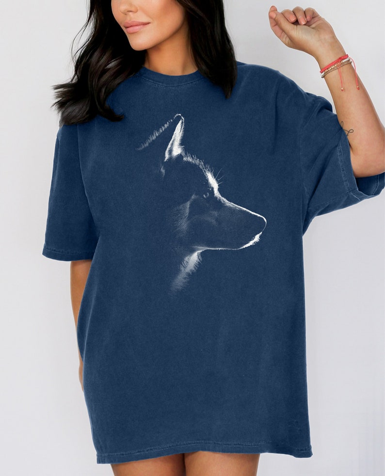 May include: A navy blue short-sleeved t-shirt featuring a white graphic print of a wolf head in profile. The design highlights the wolf's silhouette and facial features in a sketch-like style centered on the front of the garment.