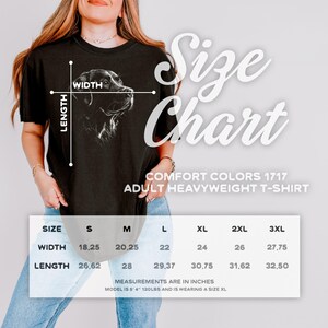 Op de afbeelding: Een zwart t-shirt met korte mouwen en een witte lijntekening van een hondenkop. De afbeelding bevat een maattabel met breedte- en lengtematen in inches voor de maten S tot 3XL, gelabeld als Comfort Colors 1717 Adult Heavyweight T-Shirt.