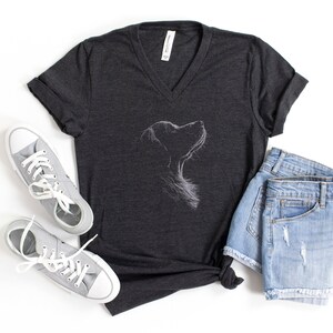 以下が含まれることがあります： ダークグレーのヘザーVネックTシャツ。上を見上げる犬の横顔が白い線画で描かれています。Tシャツの横には、白い靴紐が付いたライトグレーのキャンバススニーカーと、青いデニムのショートパンツが並べられています。