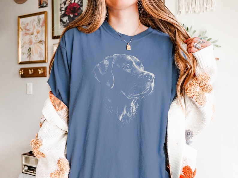 Op de afbeelding: Een blauw t-shirt met korte mouwen en een witte lijntekening van een hondenkop in profiel op de borst. Het shirt heeft een ronde hals en een relaxte pasvorm, met een gedetailleerde schets van een hondenhoofd met hangende oren.