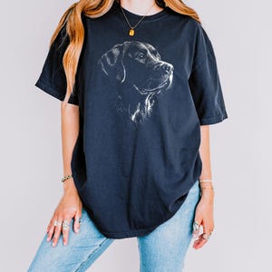 Op de afbeelding: Een donker antracietgrijs T-shirt met korte mouwen en een witte lijntekening van de kop van een Labrador retriever in profiel op de borst. Het T-shirt heeft een ronde hals en een ruimvallend, los model.