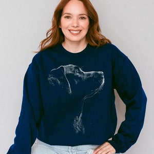 May include: A navy blue long-sleeve crewneck sweatshirt featuring a white line-art graphic of a dog in profile. The design depicts the head and neck of the canine facing toward the right side, rendered in a sketch-like style on the chest.