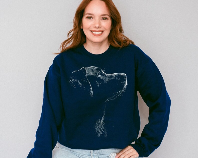 May include: A navy blue long-sleeve crewneck sweatshirt featuring a white line-art graphic of a dog in profile. The design depicts the head and neck of the canine facing toward the right side, rendered in a sketch-like style on the chest.