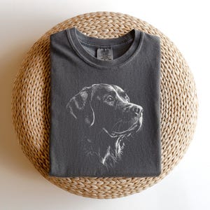 Op de afbeelding: Een antracietgrijs t-shirt met korte mouwen en een witte lijntekening van een hondenkop in profiel. Het shirt heeft een ronde hals en een zichtbaar merklabel aan de binnenkant van de kraag. Het ontwerp is in het midden geplaatst.
