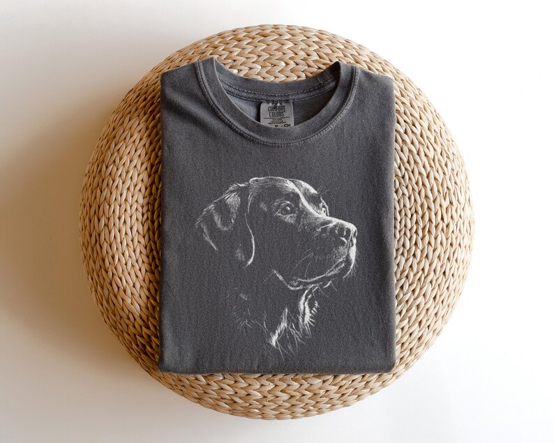Op de afbeelding: Een antracietgrijs t-shirt met korte mouwen en een witte lijntekening van een hondenkop in profiel. Het shirt heeft een ronde hals en een zichtbaar merklabel aan de binnenkant van de kraag. Het ontwerp is in het midden geplaatst.