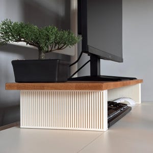 May include: A monitor stand featuring a natural wood top surface and a white, vertically ribbed base. The stand supports a black computer monitor, while a black keyboard and white computer mouse are positioned underneath the wooden platform.