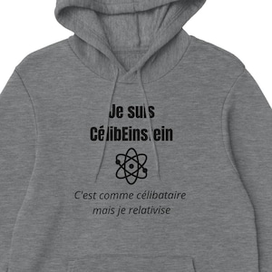 Puede incluir: Una sudadera con capucha gris con un bolsillo delantero y una capucha con cordón. La parte delantera de la sudadera presenta el texto "Je suis célibeinstein" encima de un símbolo de átomo y la frase "C'est comme célibataire mais je relativise."