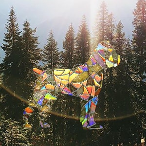 Peut inclure: Un chien en verre coloré, réalisé en vitrail, se tient dans un décor de forêt. Le chien est composé de différentes nuances de jaune, orange, rouge, bleu et vert.