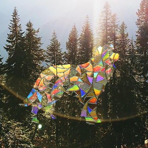 Könnte beinhalten: Eine farbige Bleiglas-Silhouette eines Wolfes vor dem Hintergrund eines Waldes mit hohen immergrünen Bäumen.