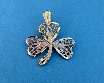 May include: A gold, silver, and rose gold tri-color shamrock pendant with a delicate filigree design.