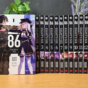 Puede incluir: Una colección de trece libros de la serie "86 EIGHTY-SIX", con el volumen uno destacado. Las portadas presentan ilustraciones de estilo anime de personajes con uniformes militares. Las lomos son negros con texto blanco. Los libros están dispuestos verticalmente.