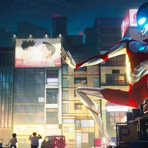 May include: A giant, red and silver superhero stands in a city street, with a large, inflatable fish-like creature in the foreground. The superhero has a blue face with a glowing blue eye. The city street is lined with buildings and signs in Japanese.