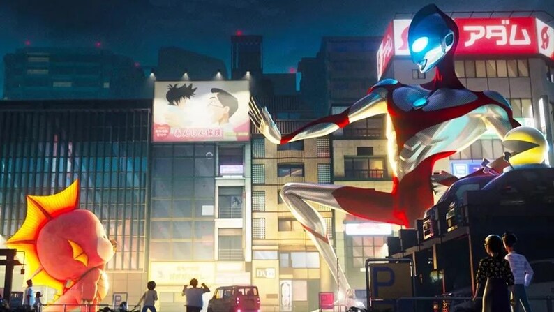 May include: A giant, red and silver superhero stands in a city street, with a large, inflatable fish-like creature in the foreground. The superhero has a blue face with a glowing blue eye. The city street is lined with buildings and signs in Japanese.