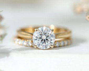 May include: A gold engagement ring set featuring a central round brilliant-cut diamond solitaire on a plain band, paired with a matching eternity band encrusted with small pavé diamonds. The jewelry is displayed with white baby's breath flowers.