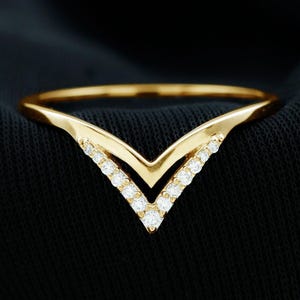 May include: A gold-colored V-shaped ring with small, clear gemstones set along the inner edges. The ring is displayed on a black fabric background, with the words "Diam Dazzle Jewels" in the upper right corner.