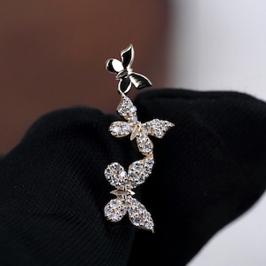 May include: A gold-toned ear climber earring featuring a vertical arrangement of three butterflies. The top butterfly is plain polished metal, while the two lower butterflies are encrusted with small, clear, sparkling white cubic zirconia stones.
