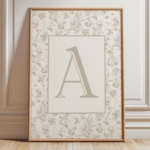 Pu&ograve; includere: Stampa incorniciata con la lettera "A". L'opera presenta uno sfondo floreale nei toni del crema e del grigio, con una cornice in legno. La lettera "A" &egrave; di colore grigio chiaro ed &egrave; centrata all'interno di un rettangolo color crema.
