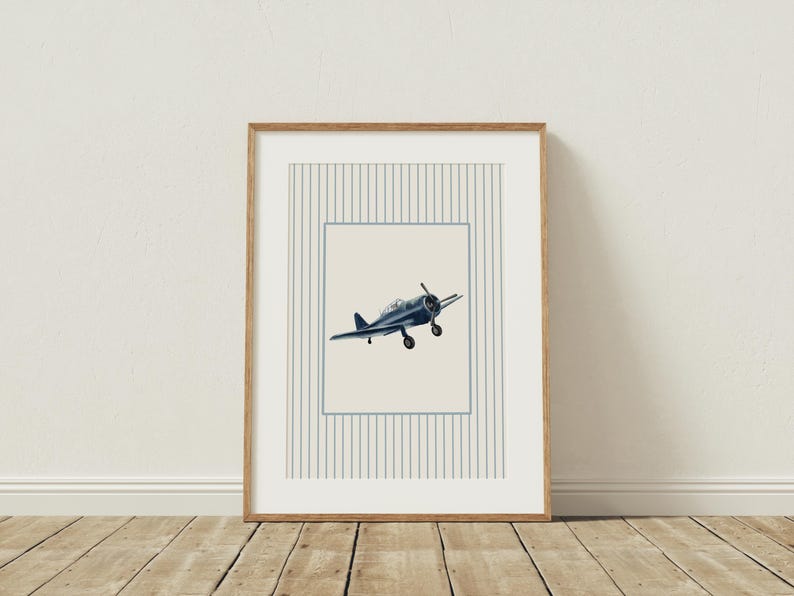 K&ouml;nnte beinhalten: Ein gerahmter Druck mit einer Illustration eines Marineblauen Vintage-Flugzeugs. Das Kunstwerk befindet sich vor einem cremefarbenen Hintergrund innerhalb eines blau linierten Rahmens und eines Streifenmusters. Der Rahmen besteht aus hellem Holz.